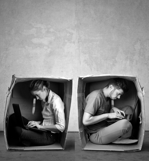 Foto en blanco y negro de un hombre y un mujer trabajando con portátil dentro de dos cajas